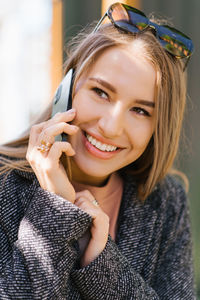 Cheerful young woman talking on a mobile phone while standing inside a cafe during the day.