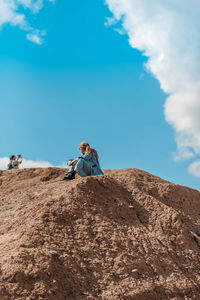 Low angle view of man sitting on rock against sky