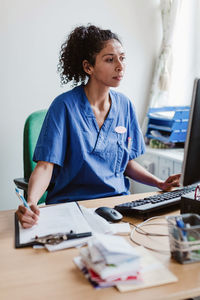 Female nurse writing report while using computer in hospital