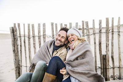 Happy couple wrapped in blanket on the beach