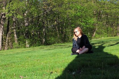 Thoughtful woman sitting on grassy field against trees