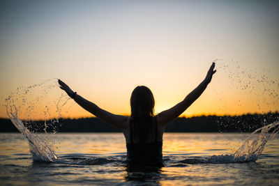 Beautiful russian girl in a long black swimsuit swims outside the city on the lake.