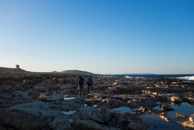Rear view of man standing on rock against clear blue sky