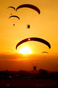 Low angle view of parachutes flying against orange sky