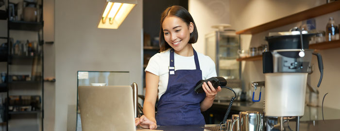 Portrait of young woman using mobile phone while standing in cafe
