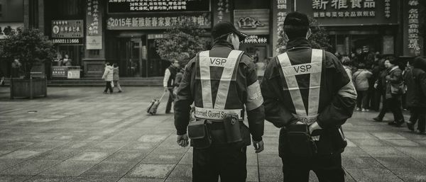 Rear view policemen looking at people standing street in city