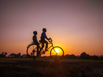 Silhouette man riding bicycle on field against sky during sunset