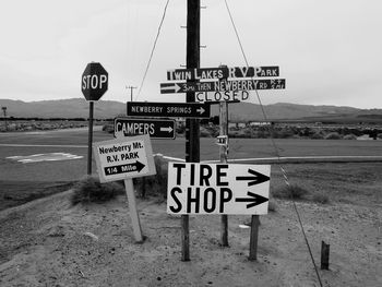 Information signs on road by field against sky