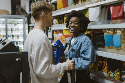 Smiling young woman doing shopping with boyfriend while standing at aisle in supermarket