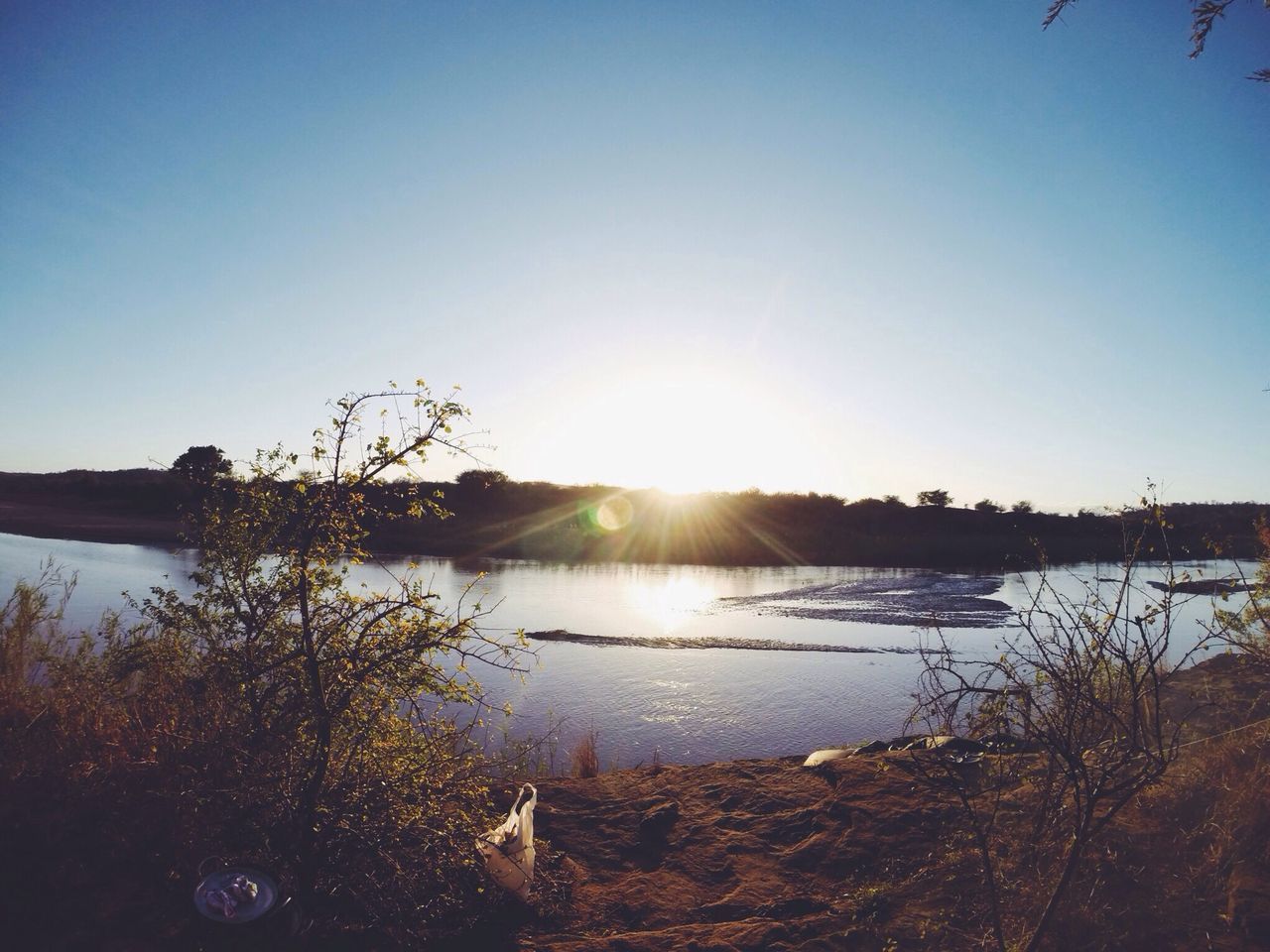 clear sky, sun, water, tranquil scene, tranquility, scenics, beauty in nature, sunlight, copy space, lake, nature, reflection, sunbeam, blue, grass, idyllic, sky, lens flare, plant, landscape