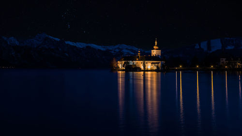 Illuminated building by lake against sky at night