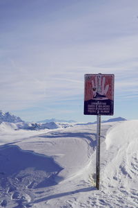 Road sign on snow covered landscape against sky