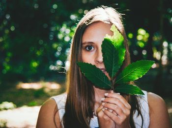 Close-up portrait of young woman holding leaves in front of face