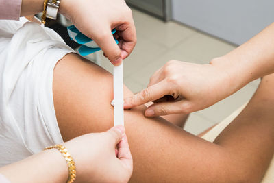 Cropped hands of female doctors applying bandage on patient arm in clinic