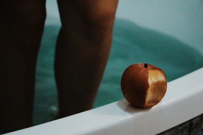 Close-up of apple against woman standing in bathtub