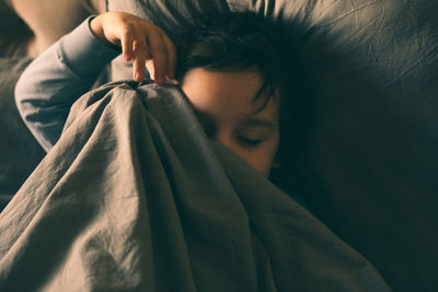 A little boy hides under the covers in bed and smiles.