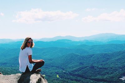 Portrait of woman sitting on mountain against sky