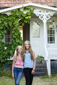 Full length of a smiling woman standing against house