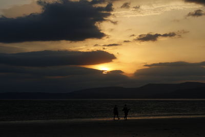 Silhouette people on beach against sky during sunset