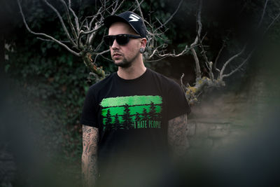 Portrait of young man wearing sunglasses standing against plants