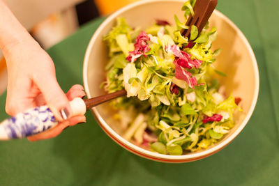 Cropped hand of woman making salad in bowl on table