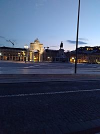 Illuminated city street against sky at dusk