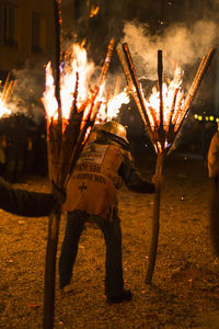 Rear view person holding burning wood on land at night