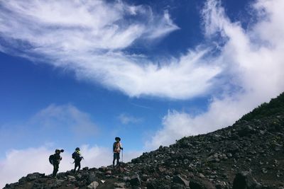 Low angle view of people climbing on mountain against cloudy sky