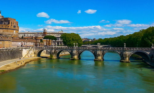 Arch bridge over river against sky in city