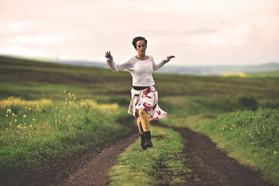 Portrait of happy woman jumping on field against sky