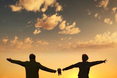 Low angle view of silhouette people with arms outstretched standing against sky during sunset