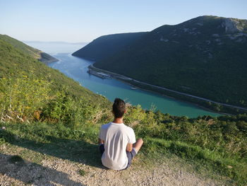 Rear view of woman sitting on mountain against sky