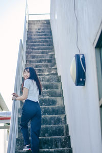 Full length of young woman climbing stairs while holding railing at building terrace