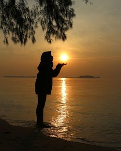 Silhouette person standing at beach during sunset