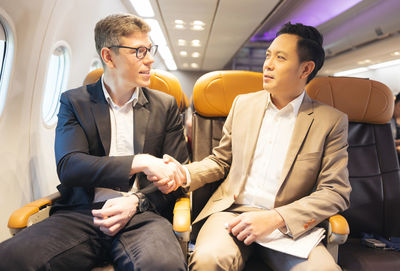 During a flight, a businessman in formal attire and glasses works with a friend near the window