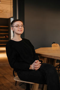 Young woman with short hair in eyeglasses and black sweater sitting at the table in office