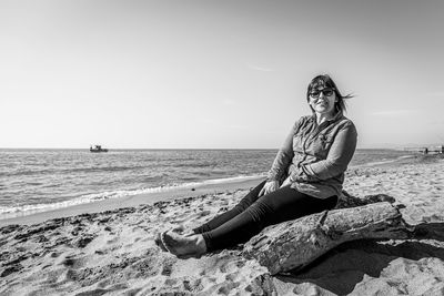 Woman sitting on beach by sea against sky