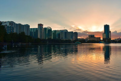 Scenic view of river by buildings against sky during sunset