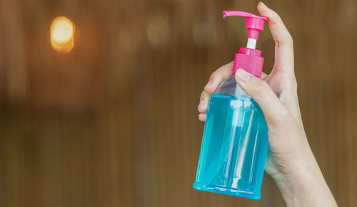 Close-up of hand holding bottle against pink wall