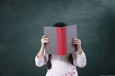 Girl reading book while standing by blackboard