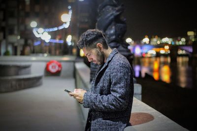 Side view of man using mobile phone in city at night