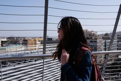 Side view of young woman standing against railing