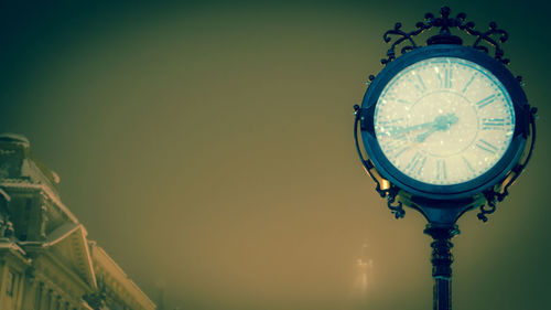 Low angle view of illuminated clock against sky