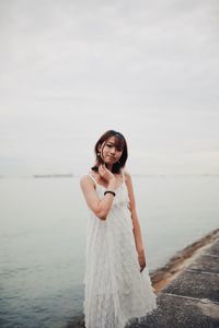 Portrait of young woman standing by sea against sky