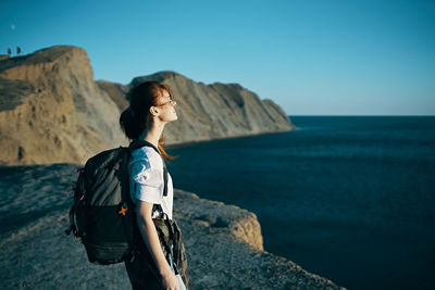 Man standing on rock by sea against sky