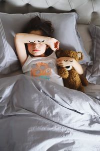 Directly above shot of girl sleeping with teddy bear on bed at home