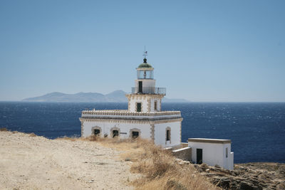 Lighthouse by sea against clear blue sky