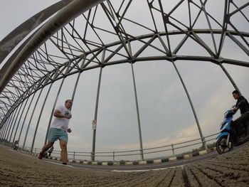 Low angle view of man walking on bridge against sky