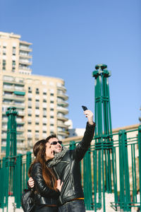 Portrait of young woman using mobile phone against sky