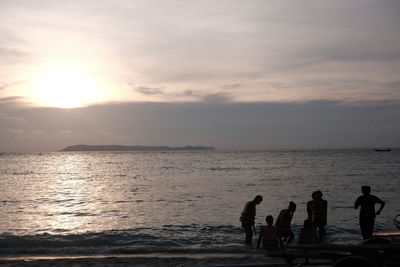Silhouette people on beach against sky during sunset